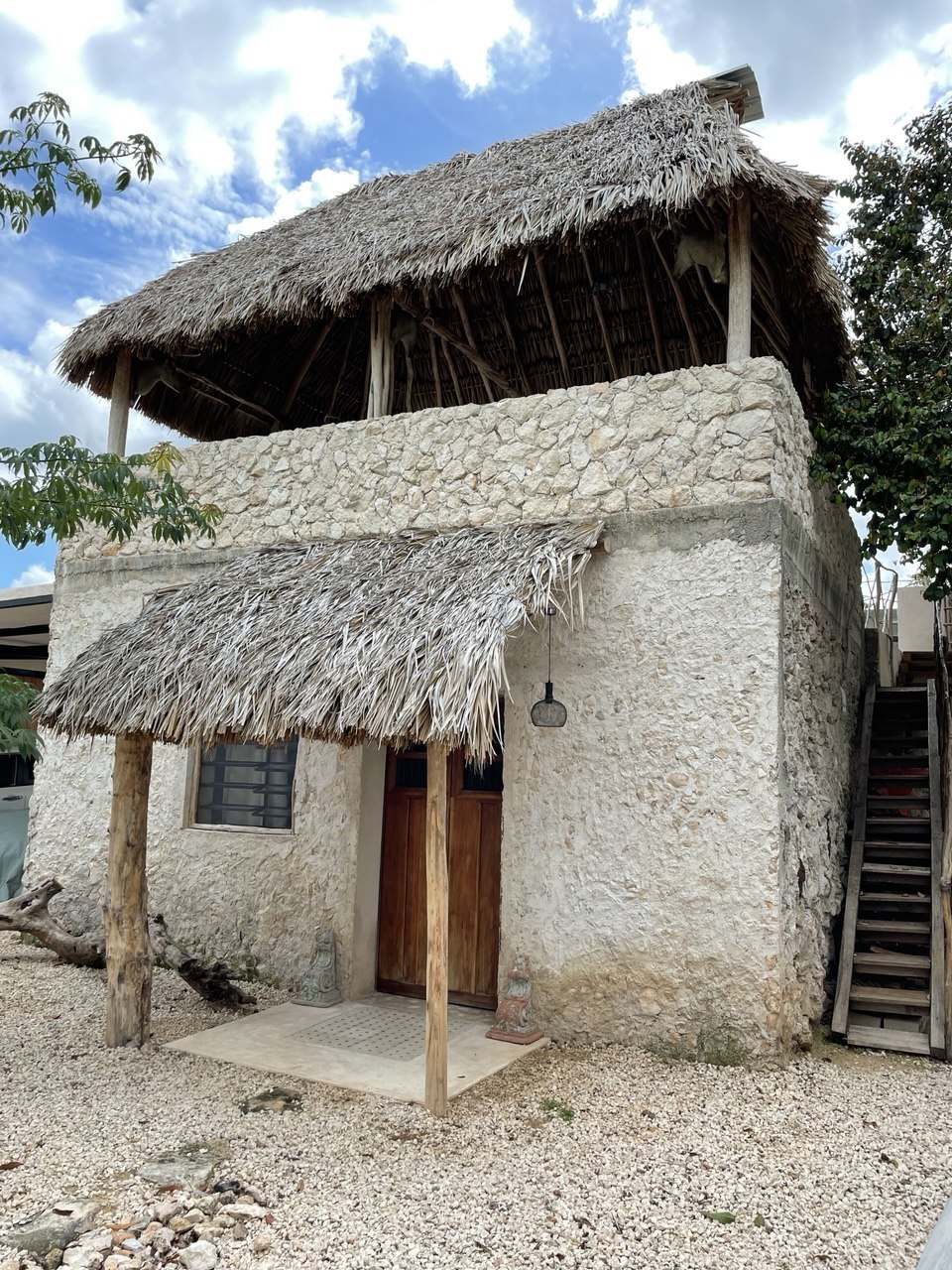 Casa de dos pisos con paredes de piedra, techo de paja y escalera exterior de madera.