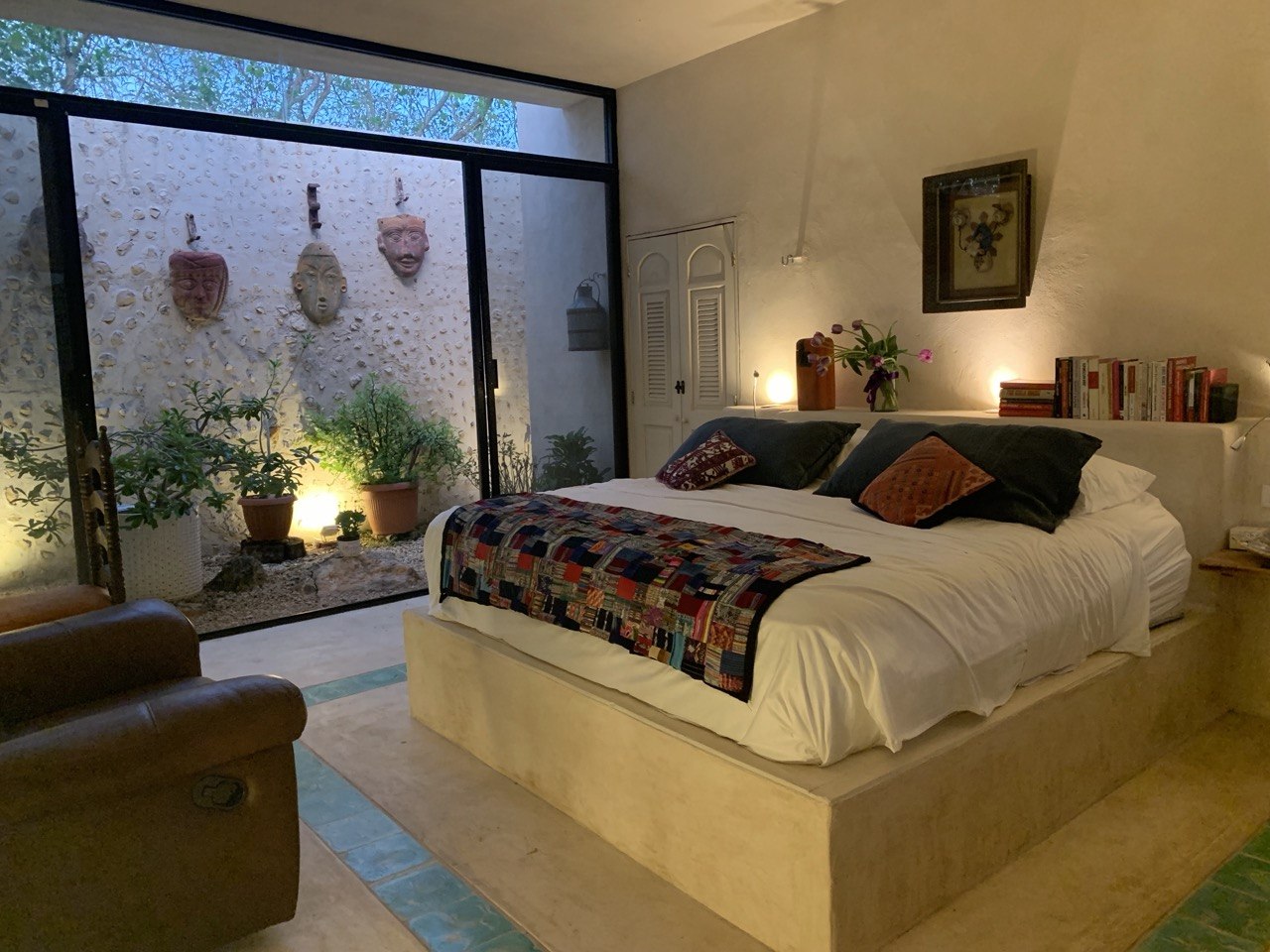 Recámara con cama doble, sillón individual y vista a un patio interior con plantas.