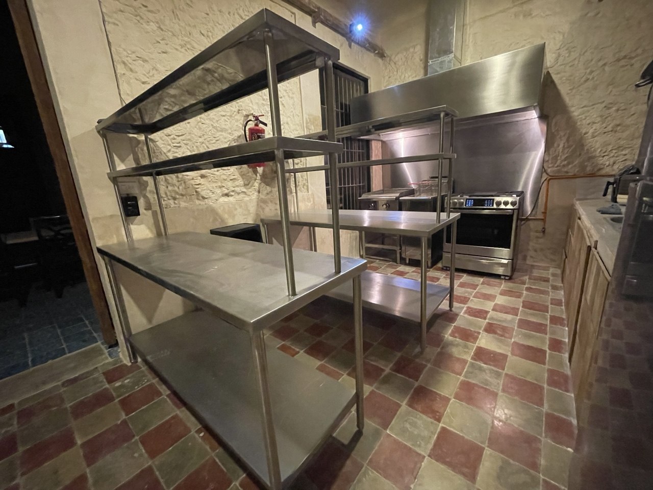 Cocina industrial con estantes de acero inoxidable, estufa y campana extractora.