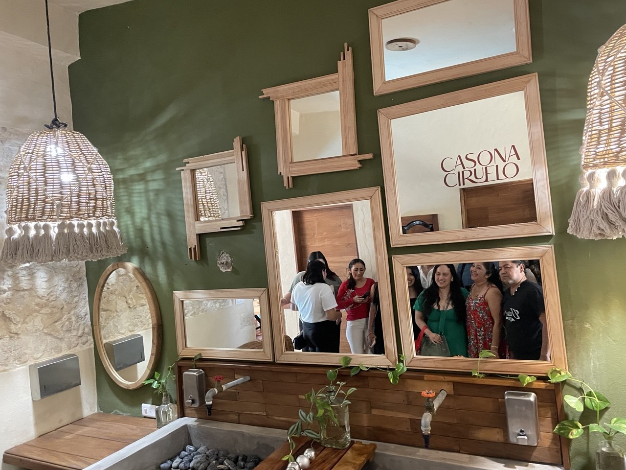 Un baño con paredes verdes, espejos de madera, lavabo de piedra y lámparas colgantes.