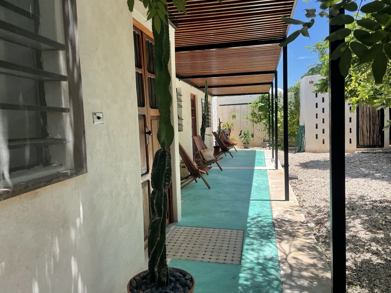 Patio exterior con piso de cemento verde, techo de pérgola y sillas de madera.
