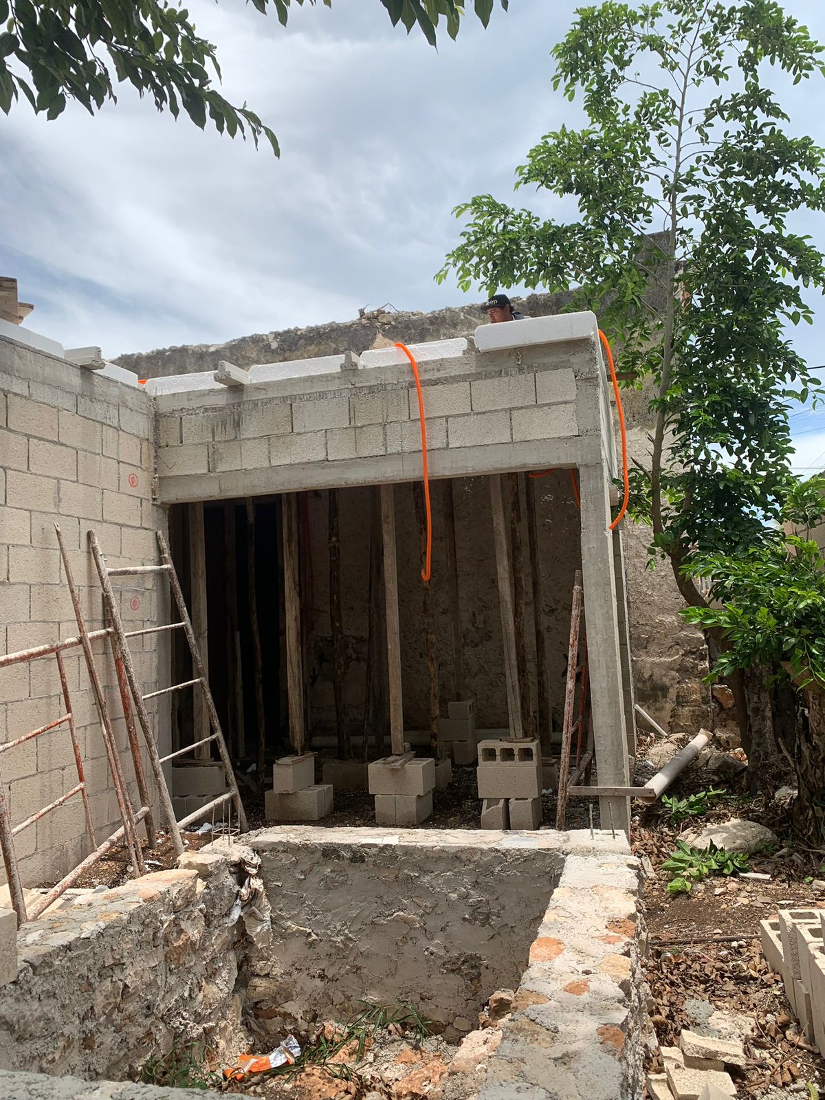 Construcción de obra negra con andamios, bloques de cemento y un árbol al fondo.