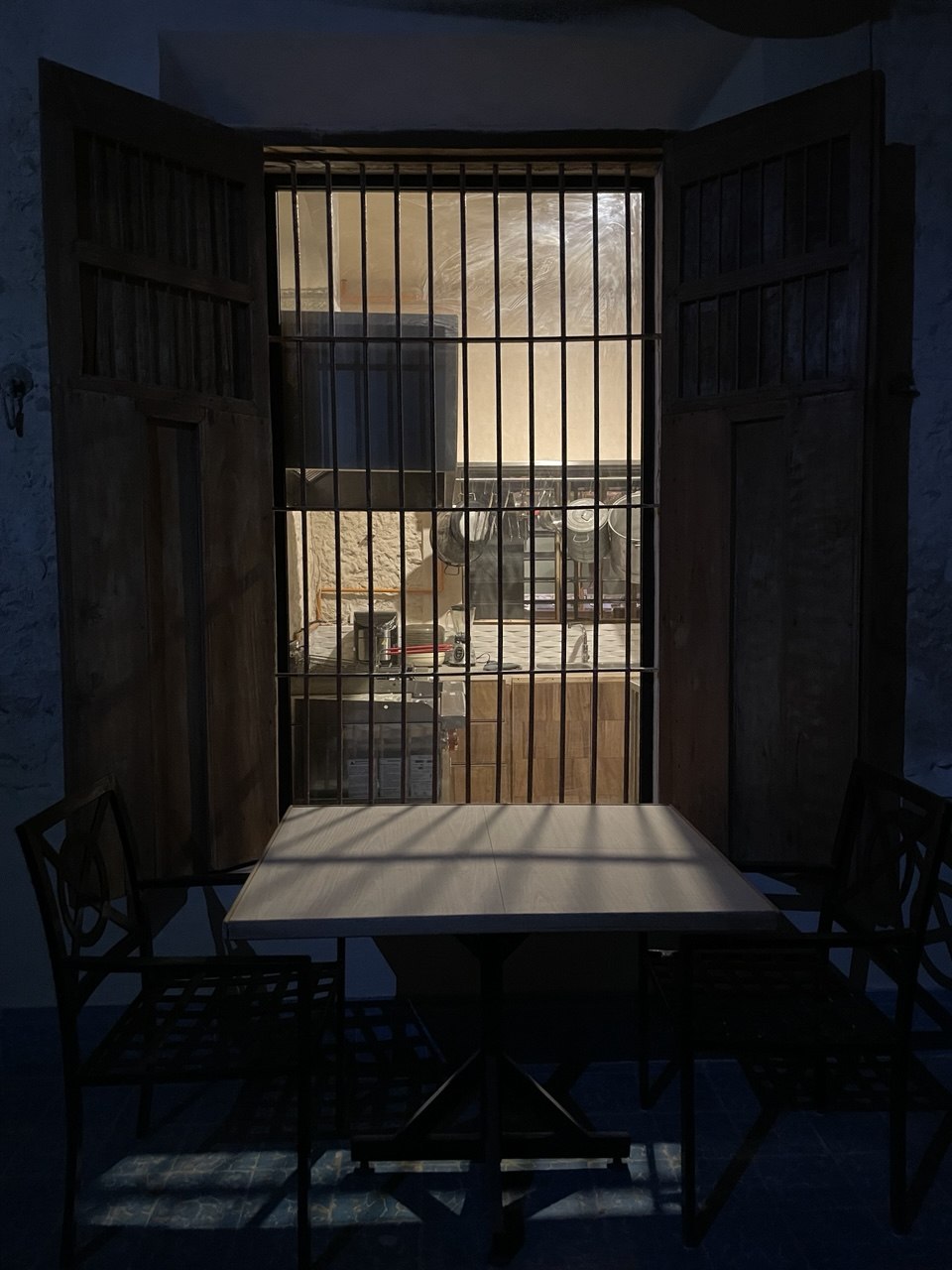 Cocina vista a través de una ventana enrejada con mesa y sillas en primer plano.
