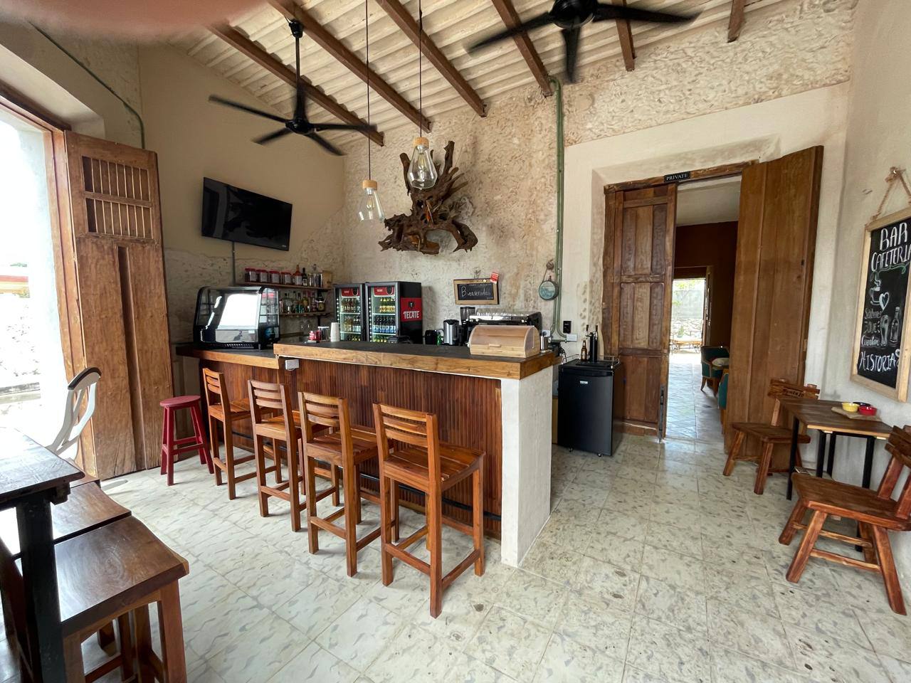 Un bar rústico con barra de madera, taburetes, mesas y sillas, y un televisor.