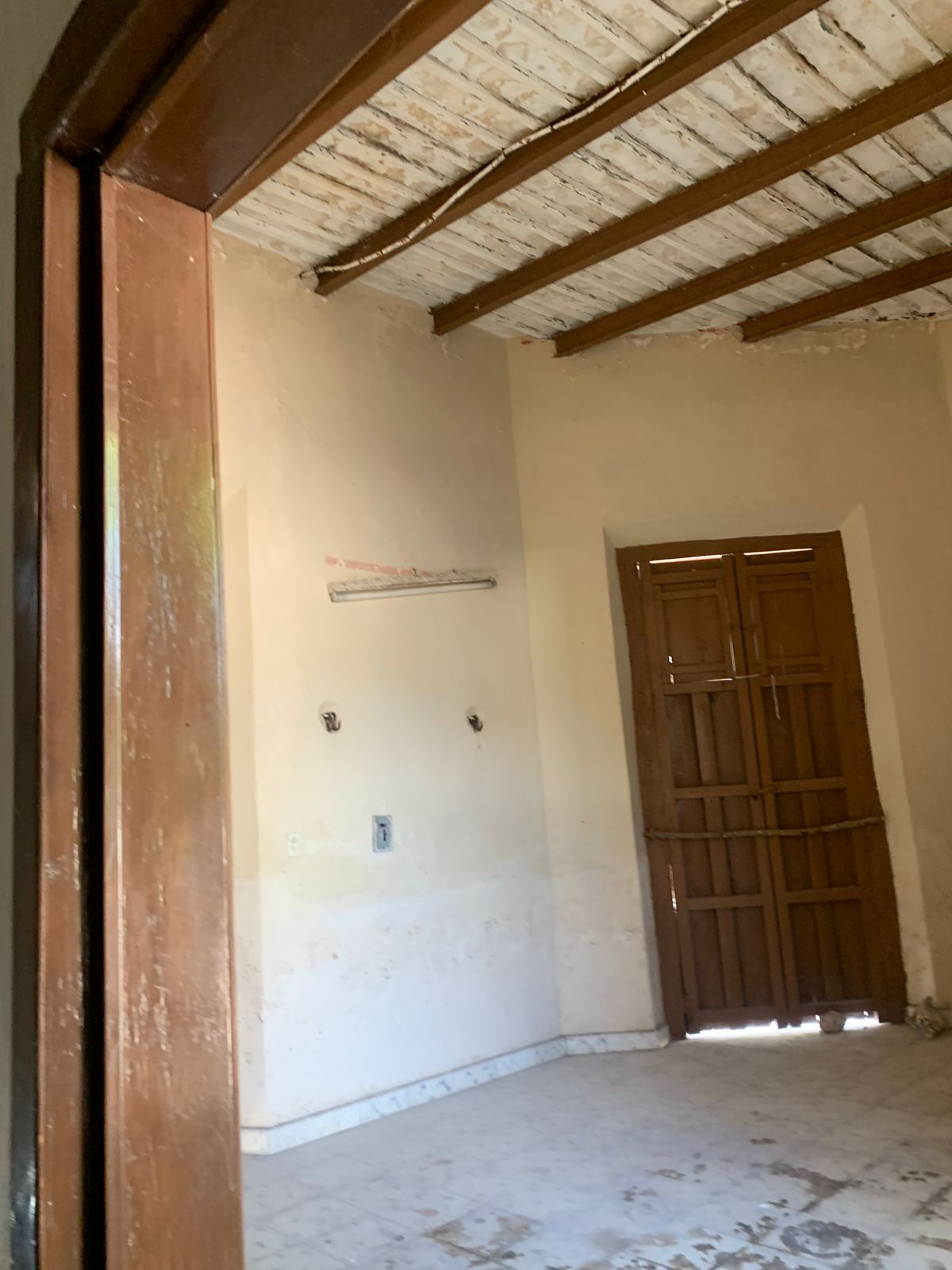 Habitación vacía con paredes claras, techo de vigas de madera y puerta de madera oscura.