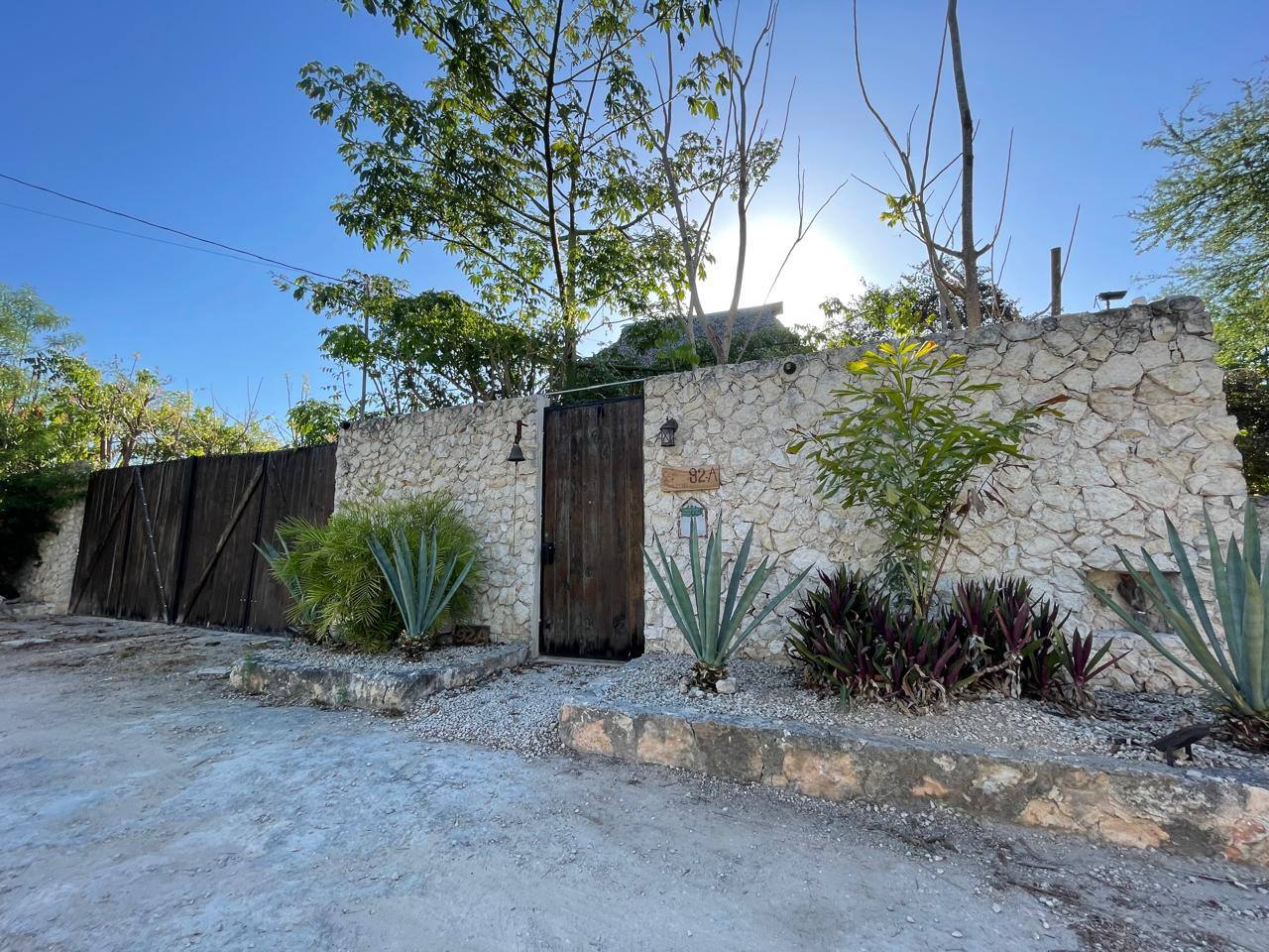 Muro de piedra con puerta de madera, plantas y un letrero con el número 92A.