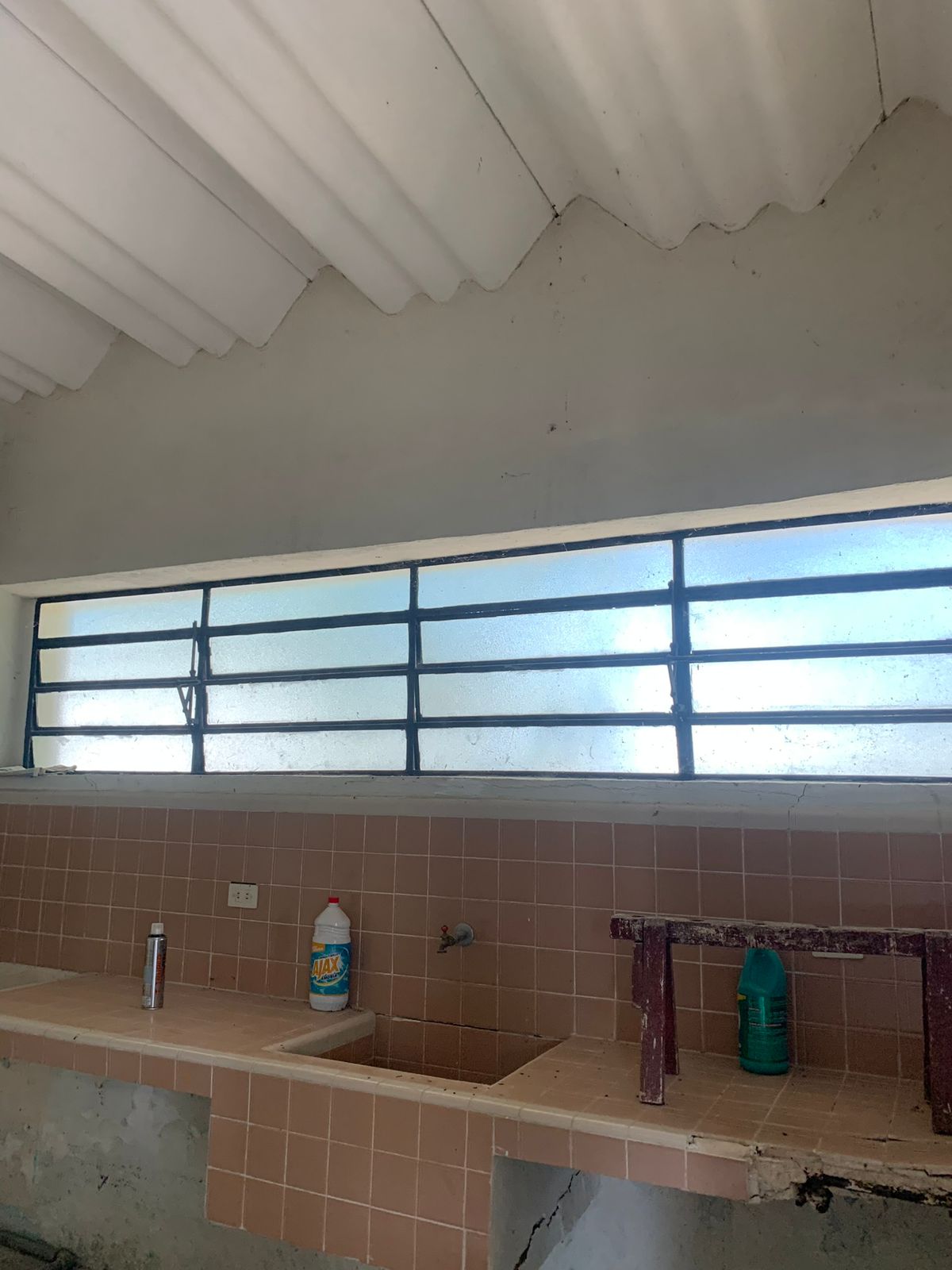 Cocina rústica con azulejos rosas, fregadero doble y ventana horizontal con rejas.