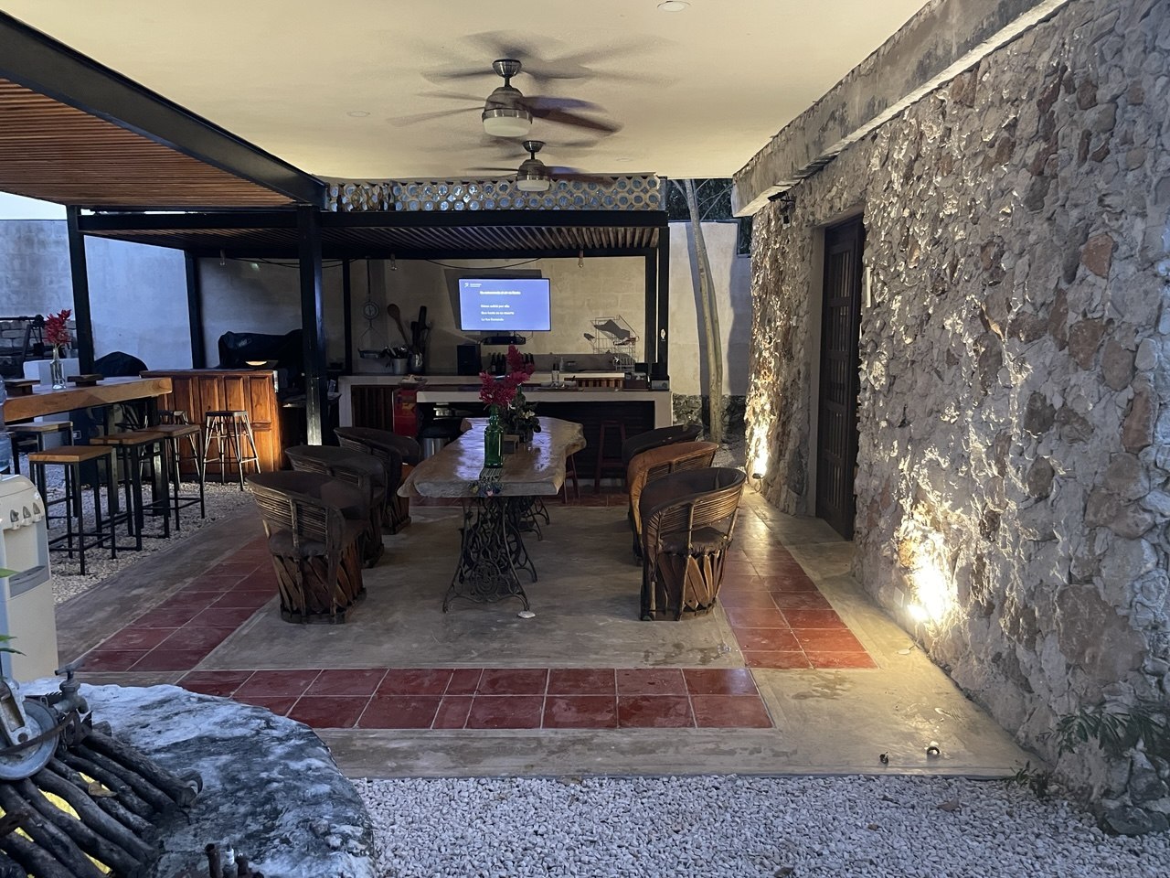 Patio exterior con comedor, barra, cocina y pared de piedra iluminada.