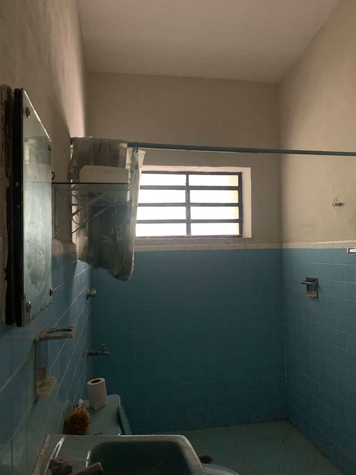 Baño con azulejos azules, ventana con rejas, cortina de ducha y lavabo.