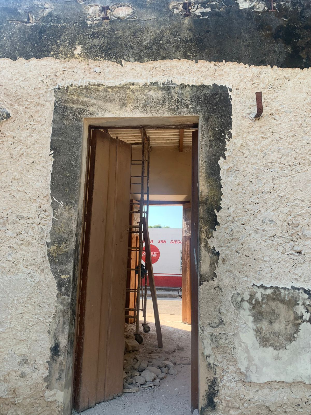 Entrada a un edificio antiguo con paredes deterioradas, puerta abierta y escalera en el interior.