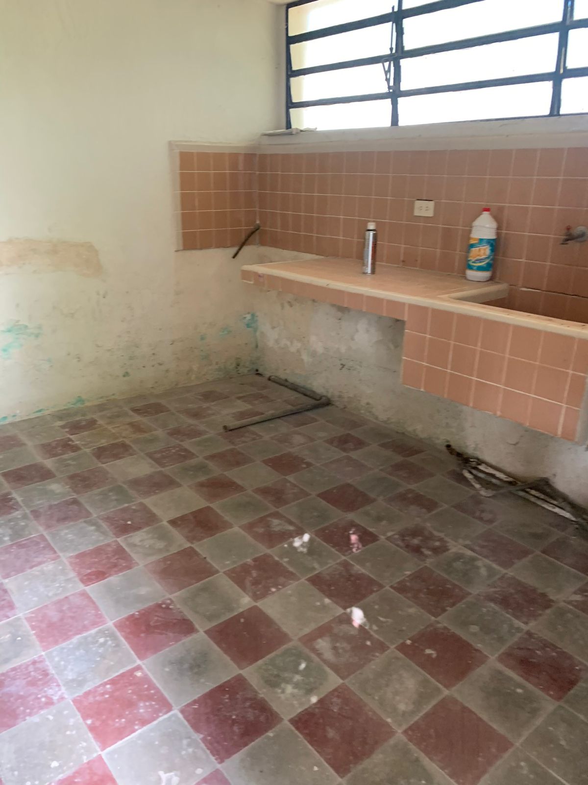Cocina vacía con azulejos de color salmón, fregadero y piso de cuadros rojos y grises.
