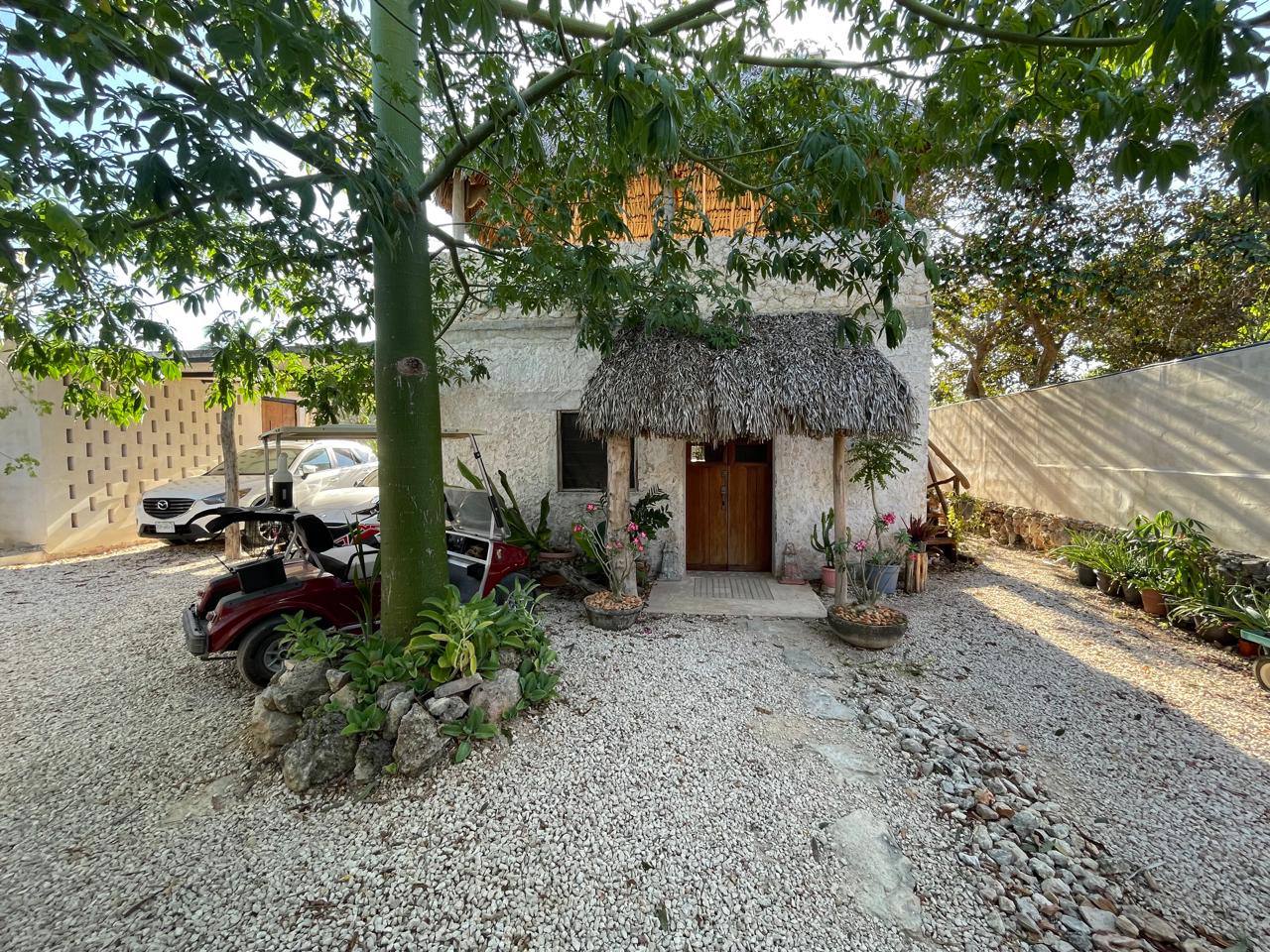 Casa de dos pisos con techo de paja, entrada de grava y carrito de golf.