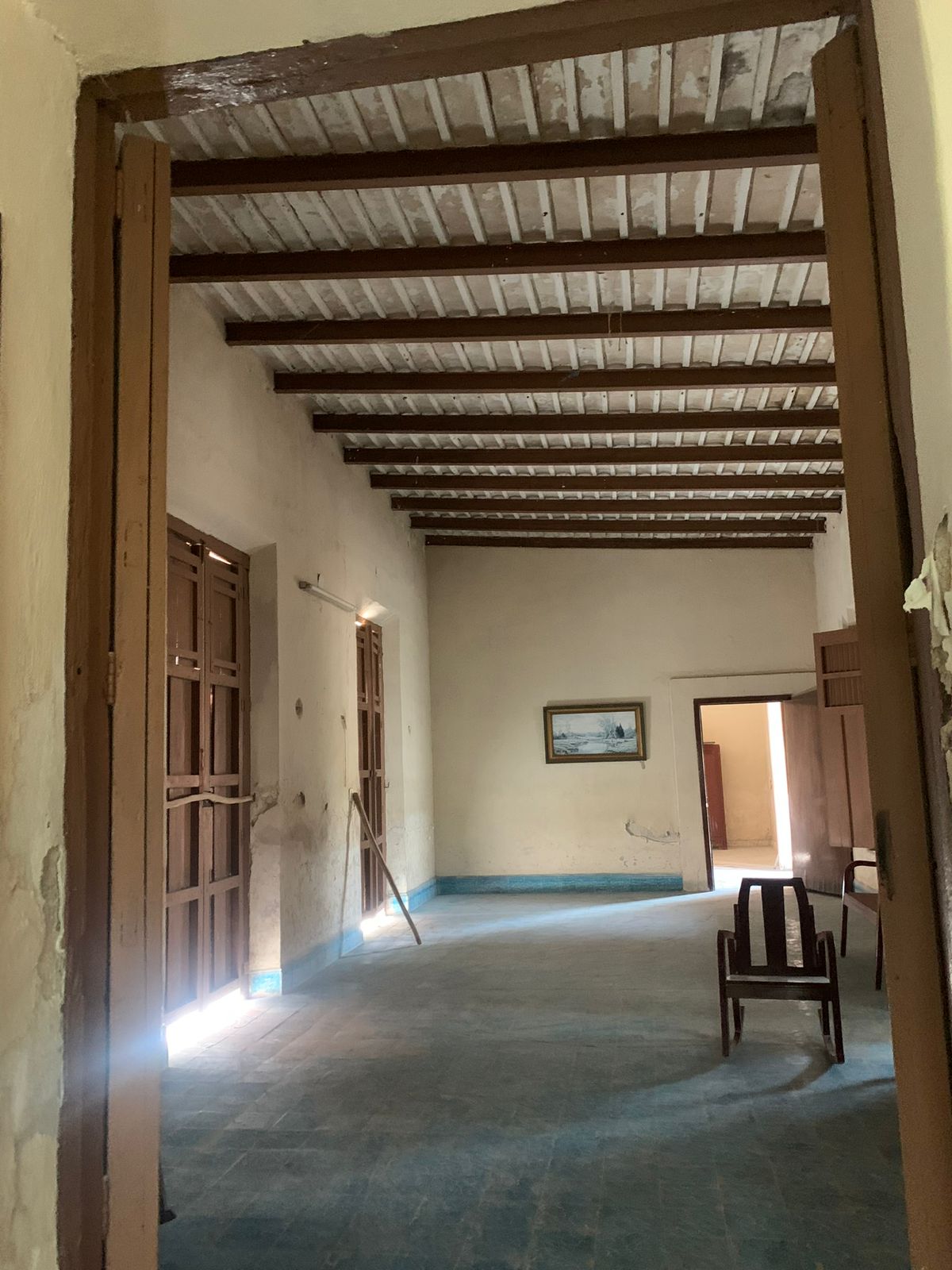 Sala vacía con techo de vigas de madera, paredes claras y piso azul.