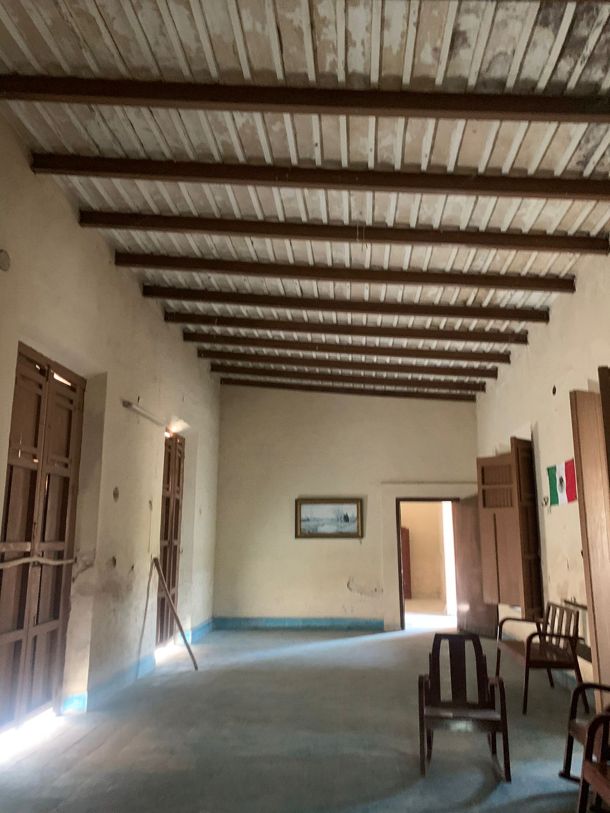Sala vacía con techo de vigas de madera, paredes claras y piso de cemento.