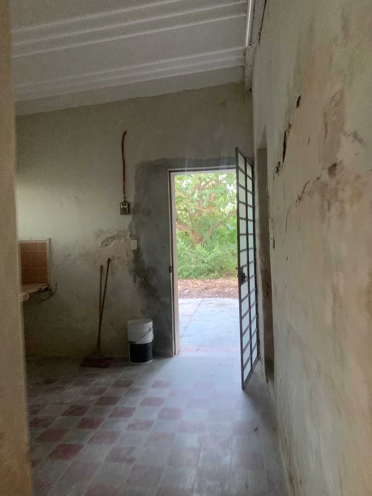 Cocina en construcción con paredes sin terminar, piso de baldosas y puerta abierta al exterior.