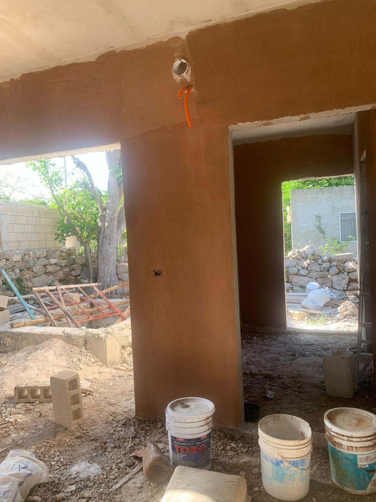 Vista de una construcción en obra negra con paredes de color terracota y materiales de construcción.